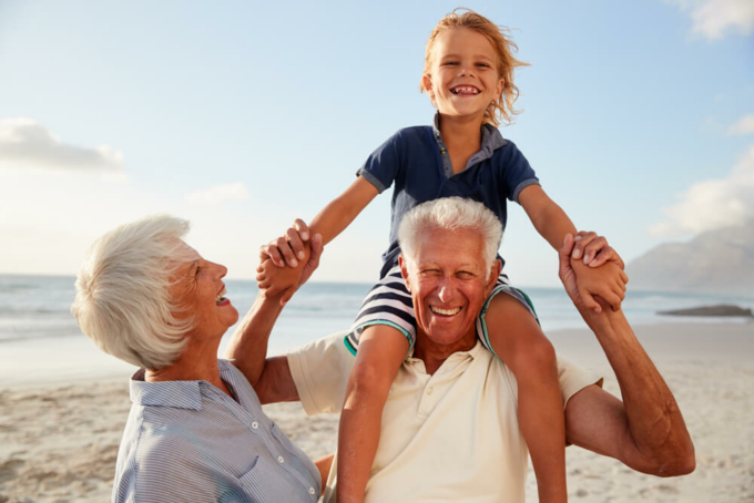Grandparents,Carrying,Grandson,On,Shoulders,On,Walk,Along,Beach